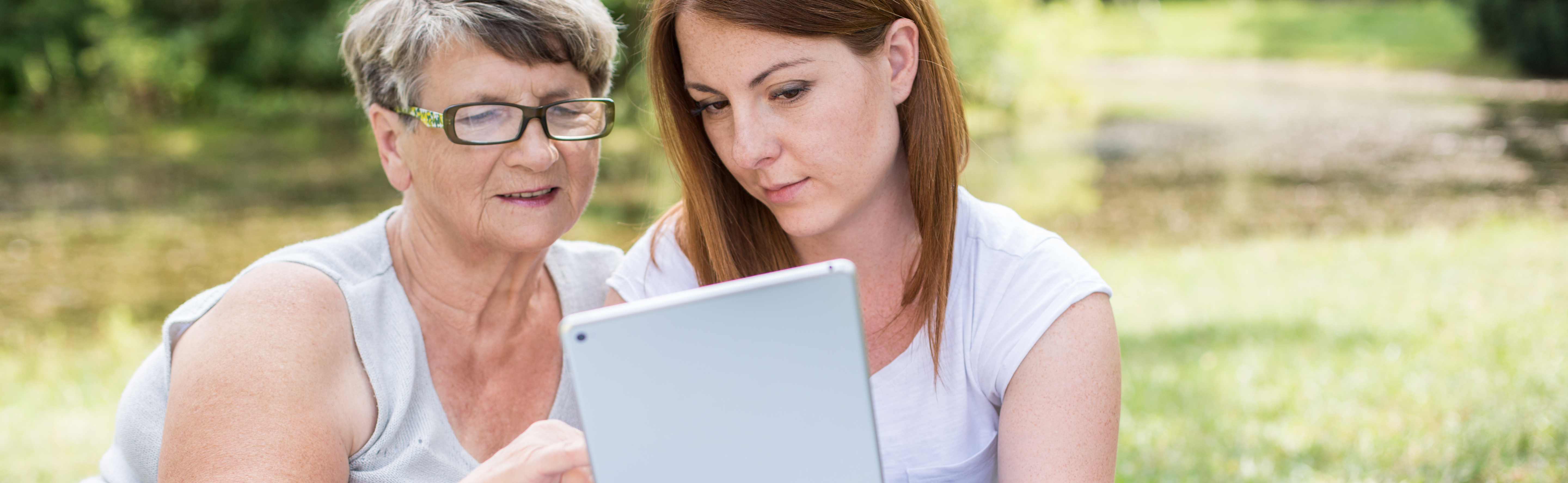 Young woman teaching grandma how to use tablet